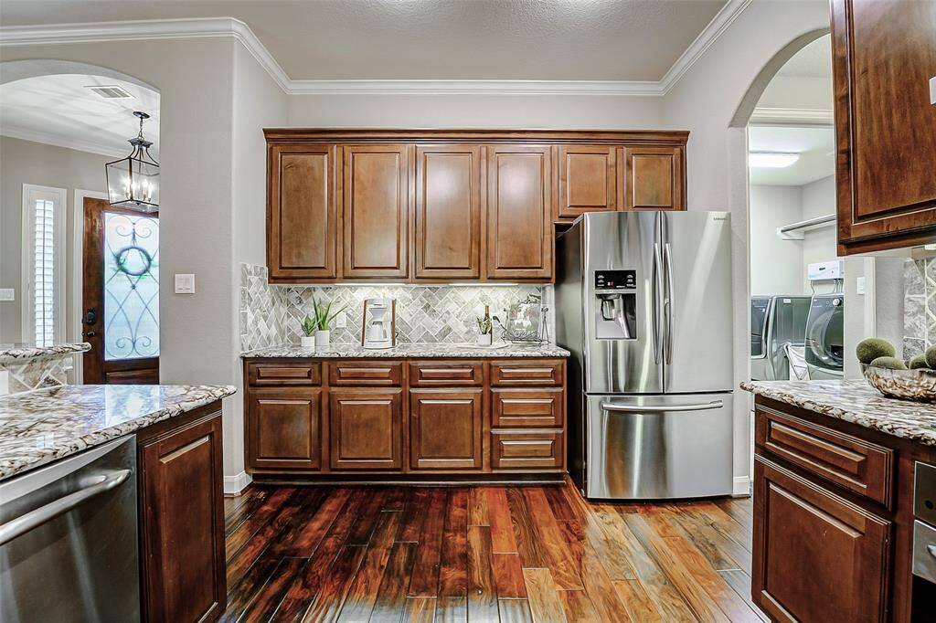 Under-cabinet lighting highlights the beautiful stone tile backsplash, adding a touch of elegance and sophistication. The accented crown molding and archway enhance the room’s openness and grandeur.