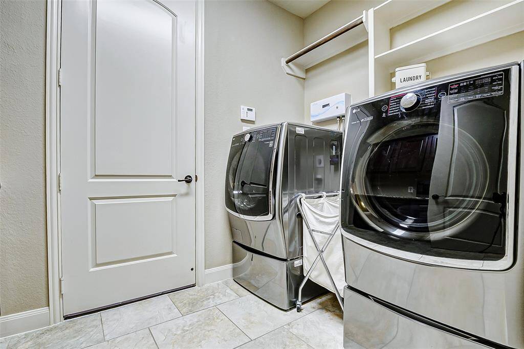 The roomy laundry area provides space for full-sized appliances. A built-in shelving unit with a hanging rod creates a designated spot for laundry essentials and delicate items.