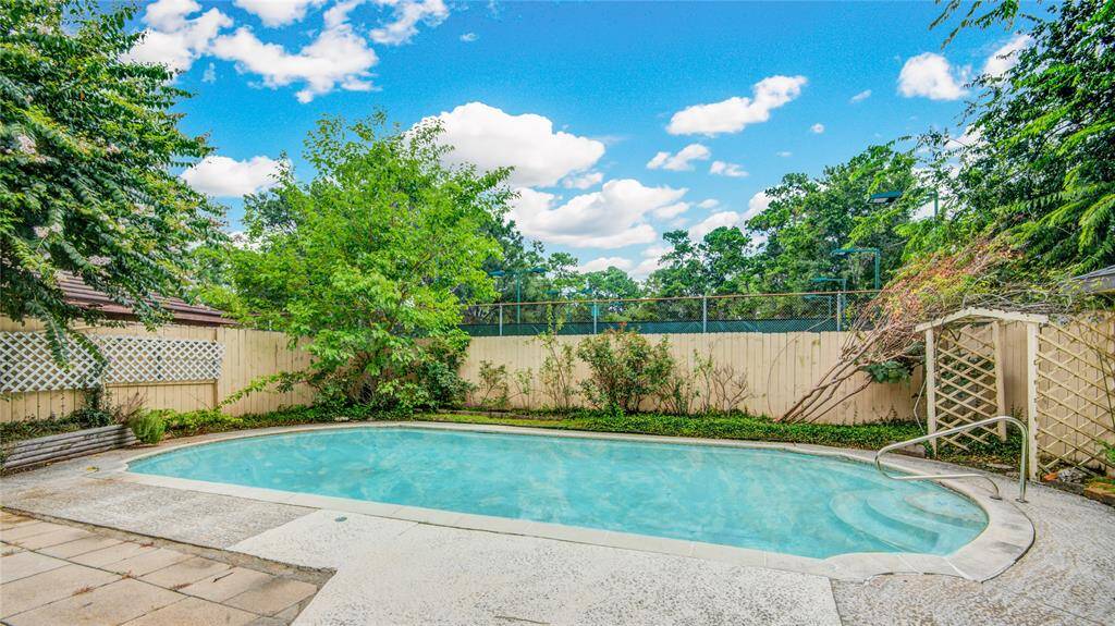 A sparkling pool glistens in the foreground, with the club tennis courts visible just beyond the fence, offering a vibrant and active backdrop.