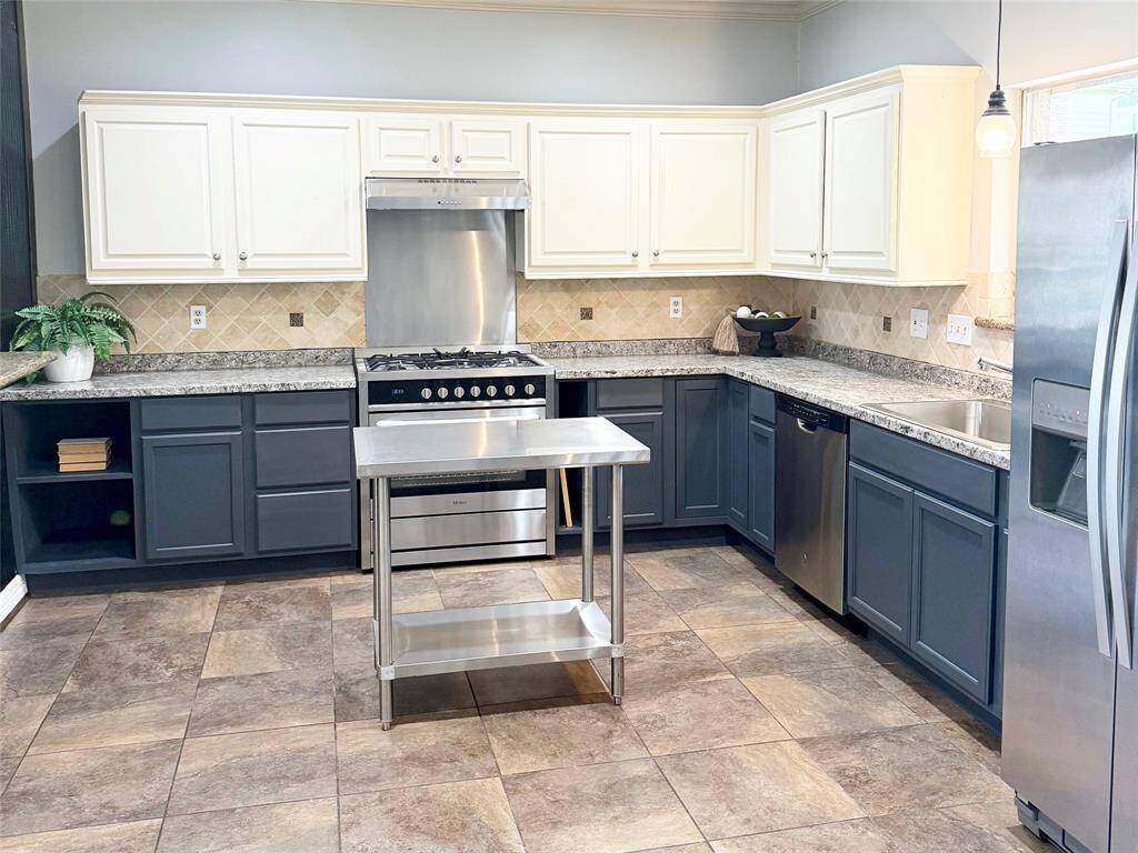 Showcasing a sleek modern update, this gourmet kitchen features freshly painted two-tone cabinetry, granite countertops, stainless steel appliances, and a stylish movable island perfect for meal prep or entertaining.