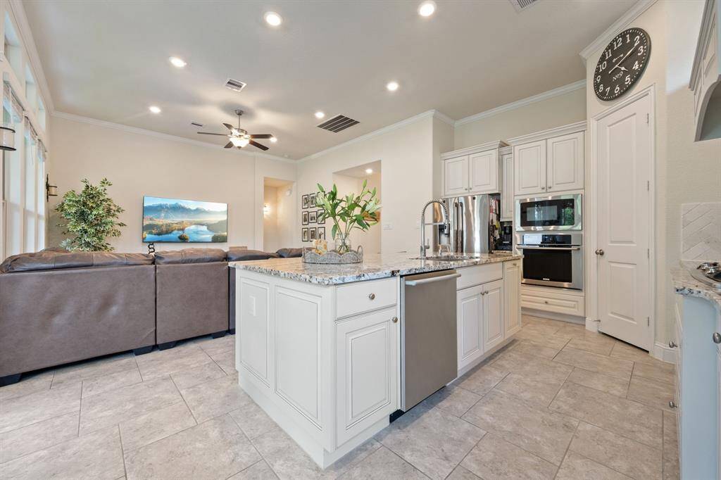 This open-concept living area features a modern kitchen with granite countertops, stainless steel appliances, and an island with a sink. Open floorpan complemented by tile flooring and recessed lighting. Perfect for entertaining.