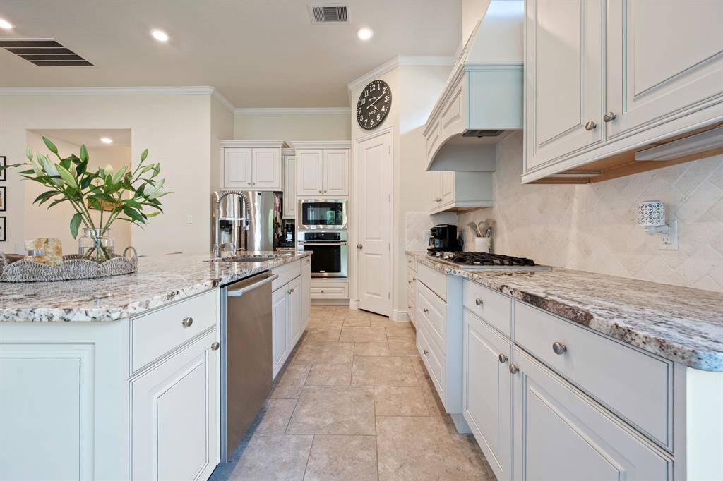 Modern kitchen with granite countertops, stainless steel appliances, and white cabinetry. Features a gas cooktop, built-in oven, and a spacious island with a sink. Bright and airy with recessed lighting and a neutral color scheme.