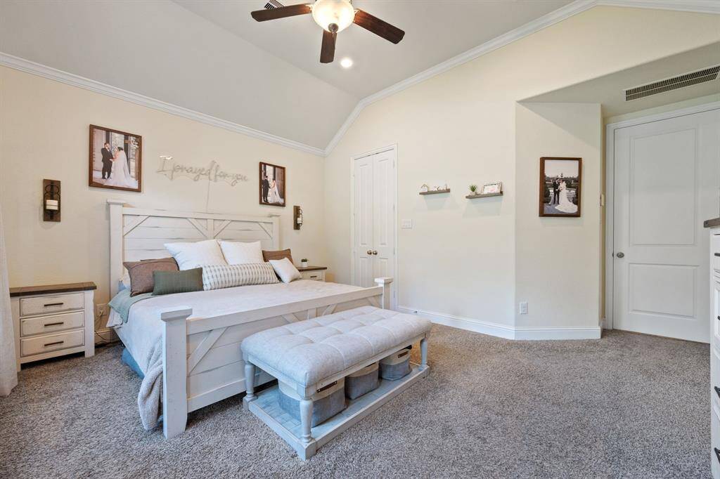 This spacious primary bedroom features a cozy carpeted floor, a ceiling fan, and soft neutral walls and a great view to the backyard.