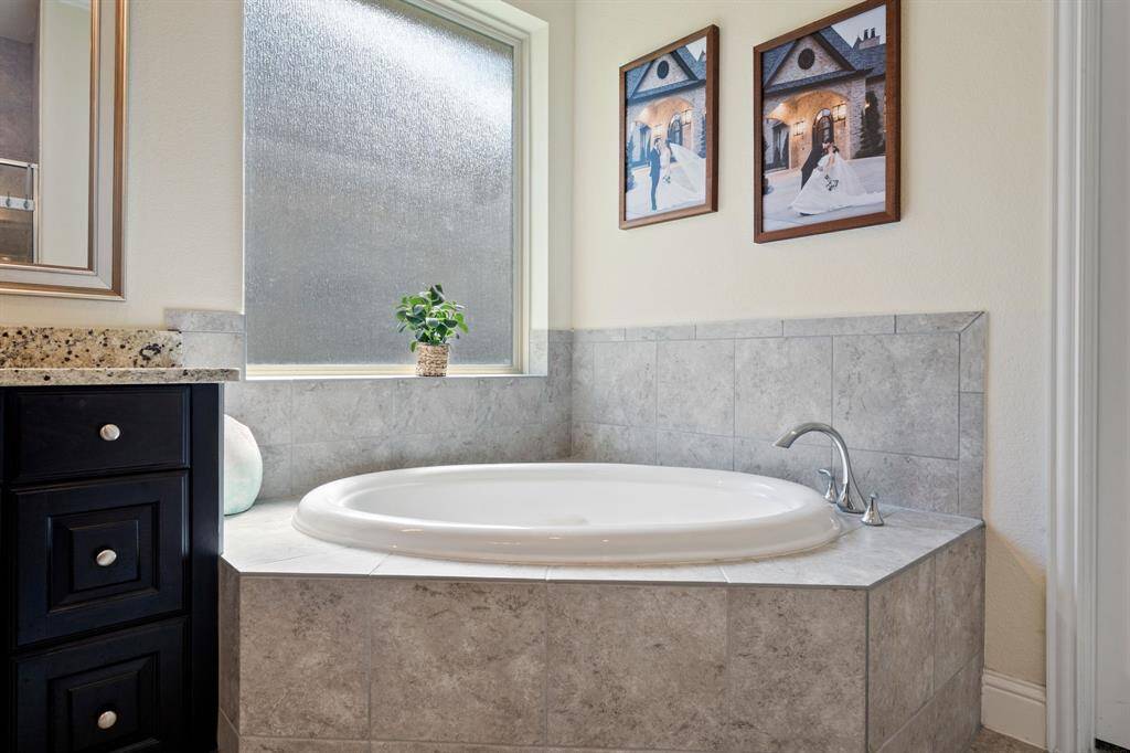 This bathroom features a cozy corner tub with elegant gray tile surround. A large frosted window provides natural light while maintaining privacy.
