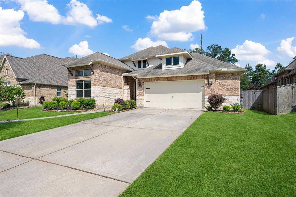 This is a modern brick house with a two-car garage, a well-maintained lawn, and a spacious driveway. It features a mix of stone and brick facade, large front windows, and a neatly landscaped front yard.