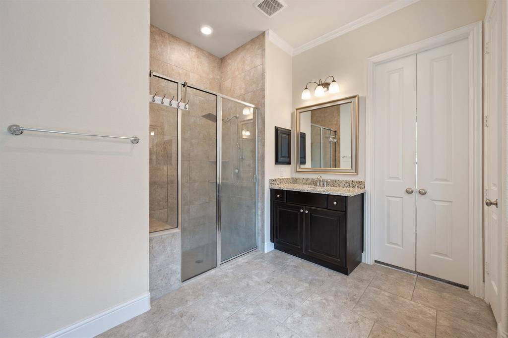 This bathroom features a spacious glass-enclosed oversized shower with elegant tile work, a granite countertop vanity, and modern lighting. The neutral tones and ample natural light create a welcoming and clean atmosphere.