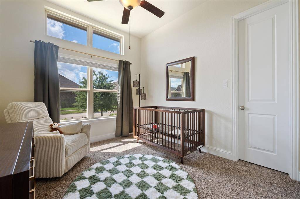 This cozy bedroom features a large window allowing natural light, neutral walls, carpeted floor, and a ceiling fan.