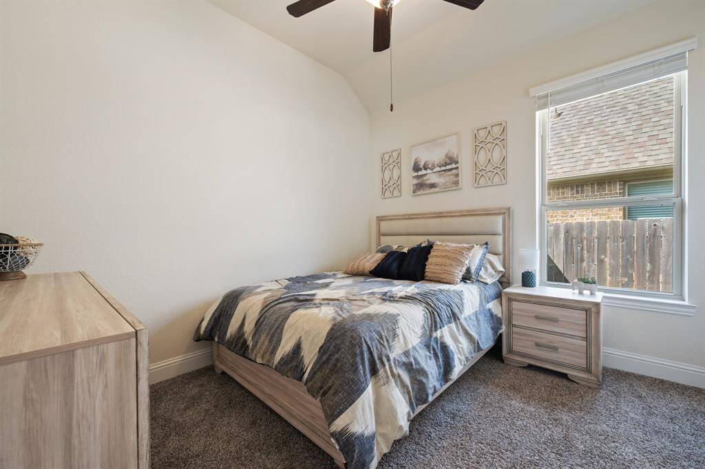 This secondary bedroom features a large window for natural light, neutral walls, and a ceiling fan.