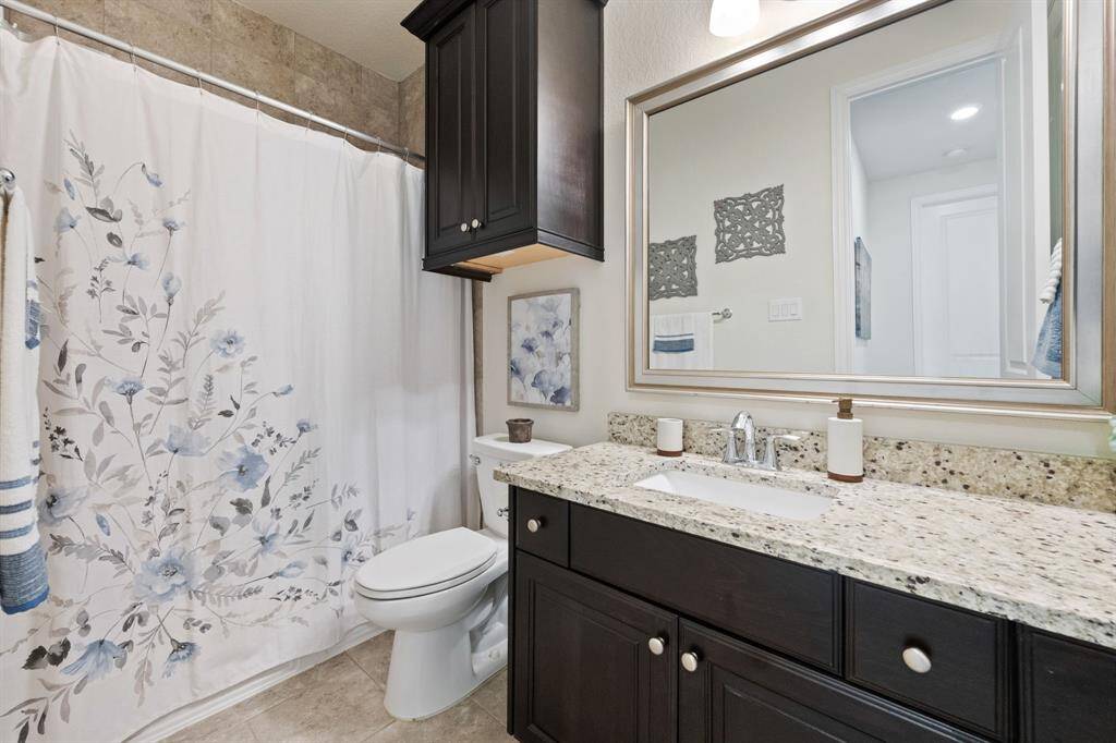 This bathroom features a sleek granite countertop with a modern undermount sink, complemented by dark wood cabinetry. Large mirror with elegant lighting, offering a bright and stylish space.