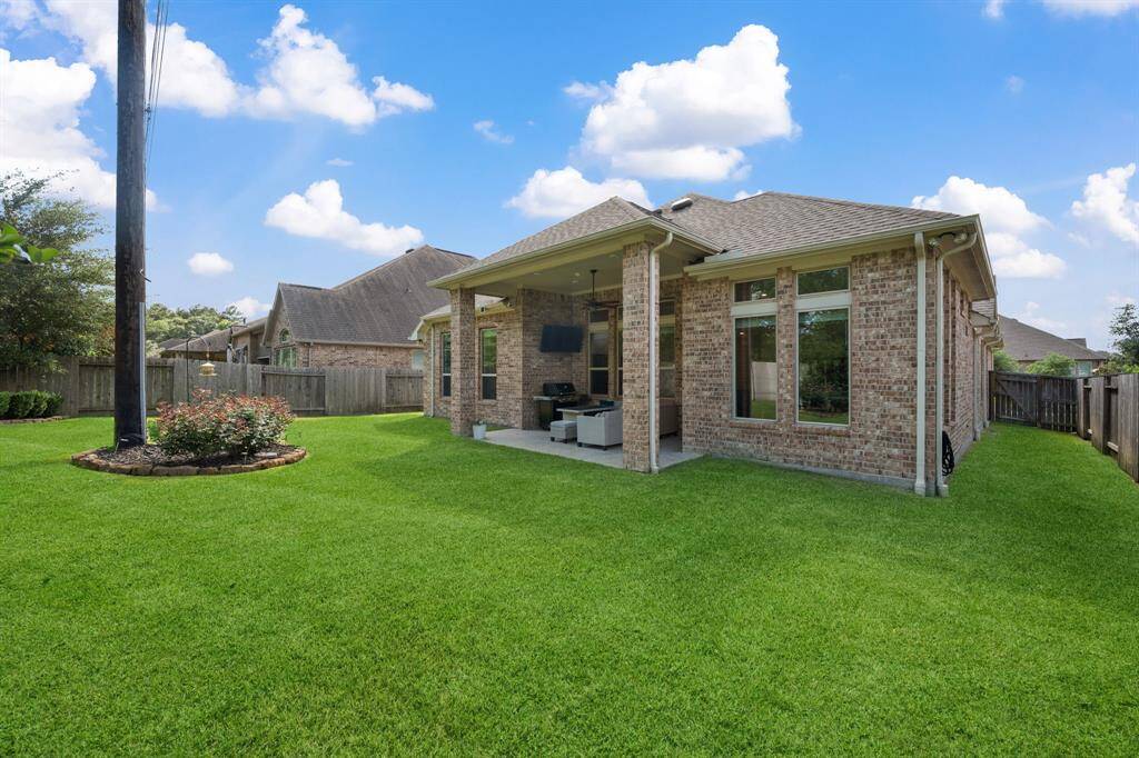 This photo shows a spacious backyard with a well-maintained lawn and a covered patio attached to this 4 sided brick home. The yard is fenced, with no neighbors behind, offering plenty of privacy.