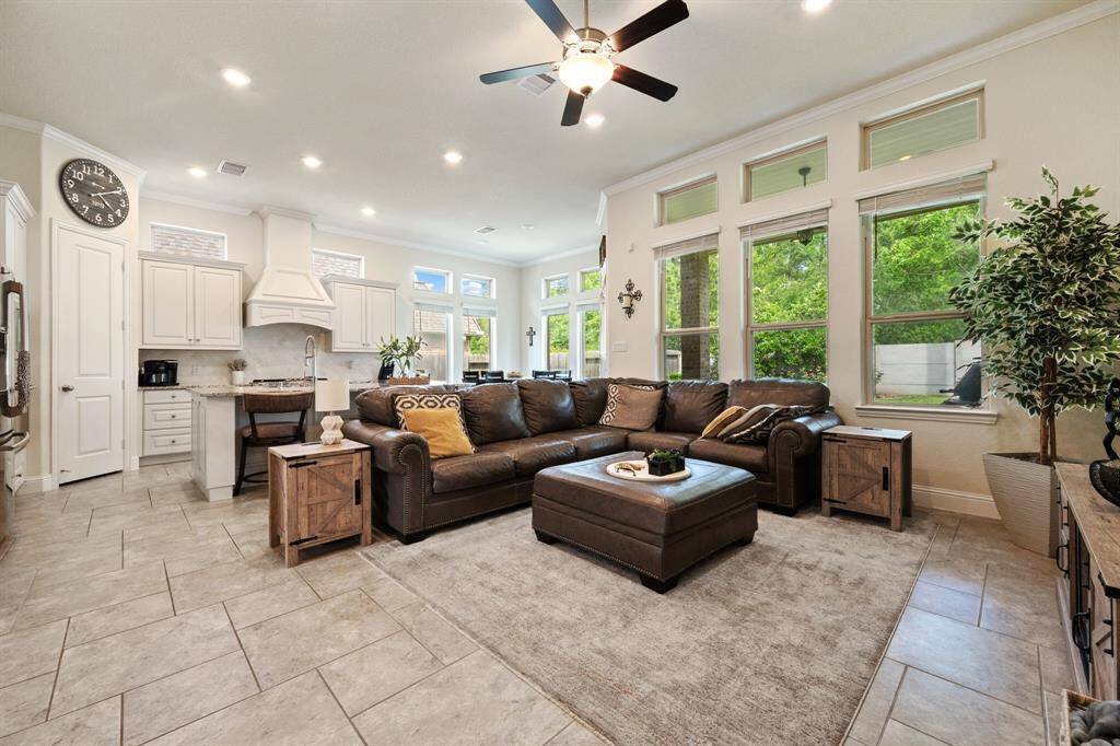 This spacious open-concept living area features a modern kitchen with white cabinetry, a large island, and stainless steel appliances. It flows into a cozy living room , large windows offering natural light, and a view of the greenery outside. The neutral tones and stylish decor create a welcoming atmosphere.