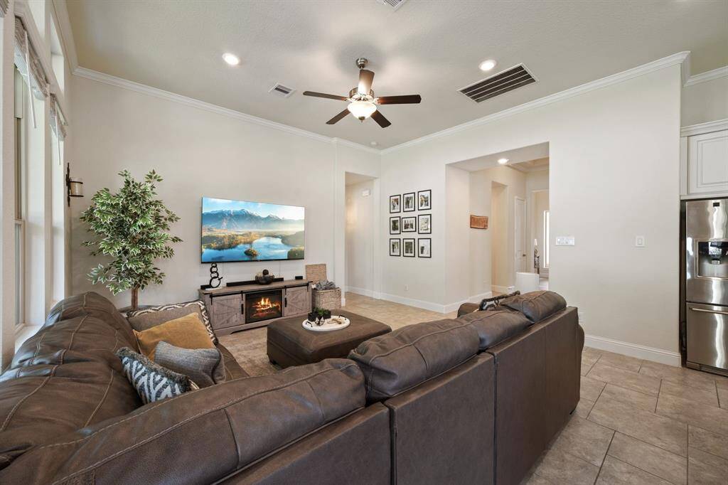 This inviting living room features bright  natural light from multiple windows, has neutral walls, and is accented with a ceiling fan. Perfect for relaxation and entertainment.
