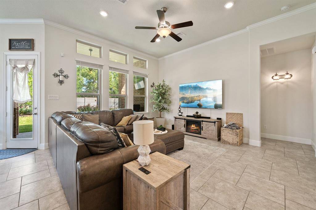 This homes showcases a bright and inviting living room with tile flooring, and a ceiling fan. Natural light pours in through multiple windows. A door leads to a backyard, creating an open, airy feel.