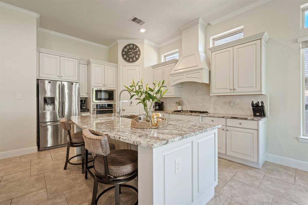 This kitchen features a spacious, modern design with light cabinetry and granite countertops. It includes a large island with seating, stainless steel appliances, and ample natural light, creating an inviting and functional space.