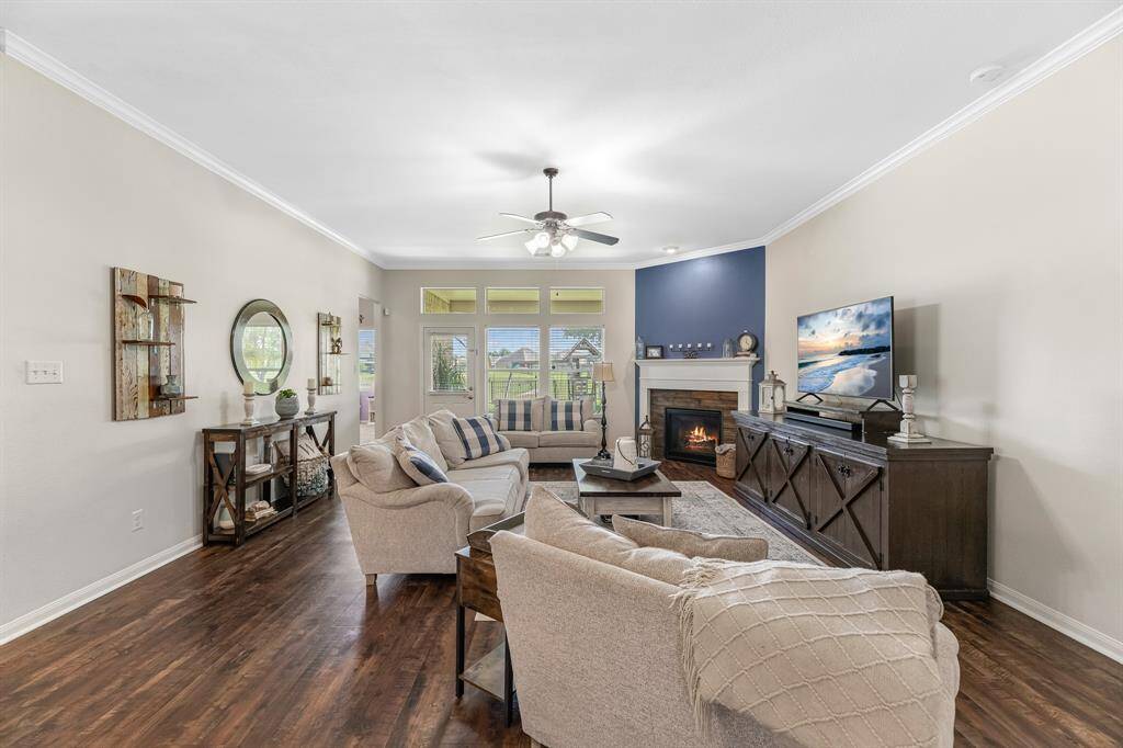 Large living area with vinyl plank flooring, crown molding, corner fireplace, and large windows looking out onto the back patio.