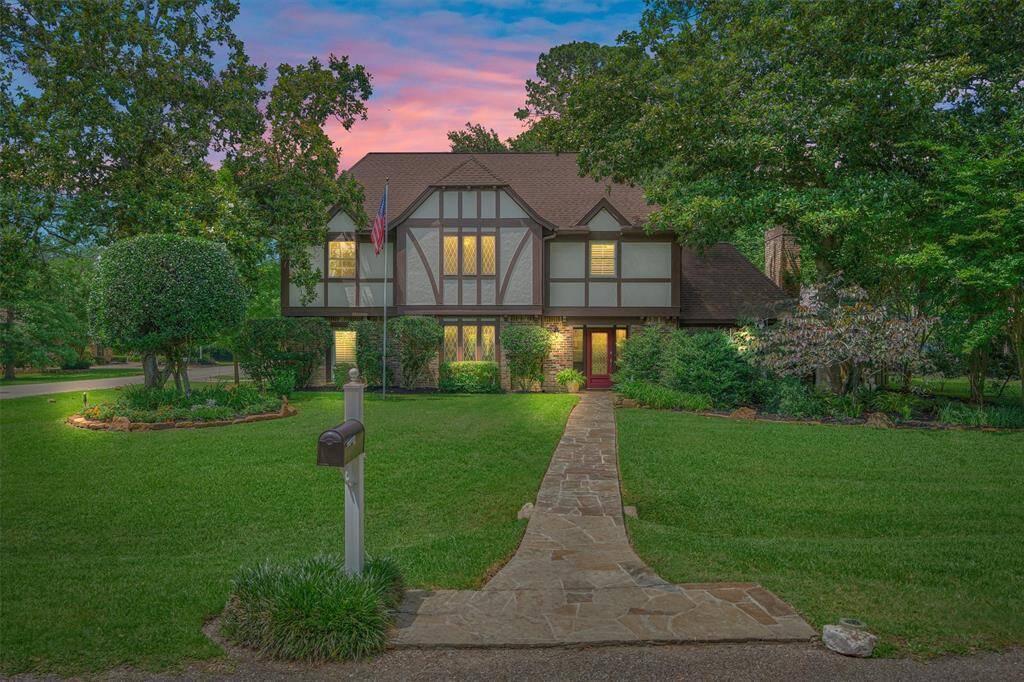 This charming Tudor-style home features a well-manicured lawn, a stone walkway, and mature trees, creating a welcoming and picturesque curb appeal. A flagpole and classic mailbox add to its traditional charm.