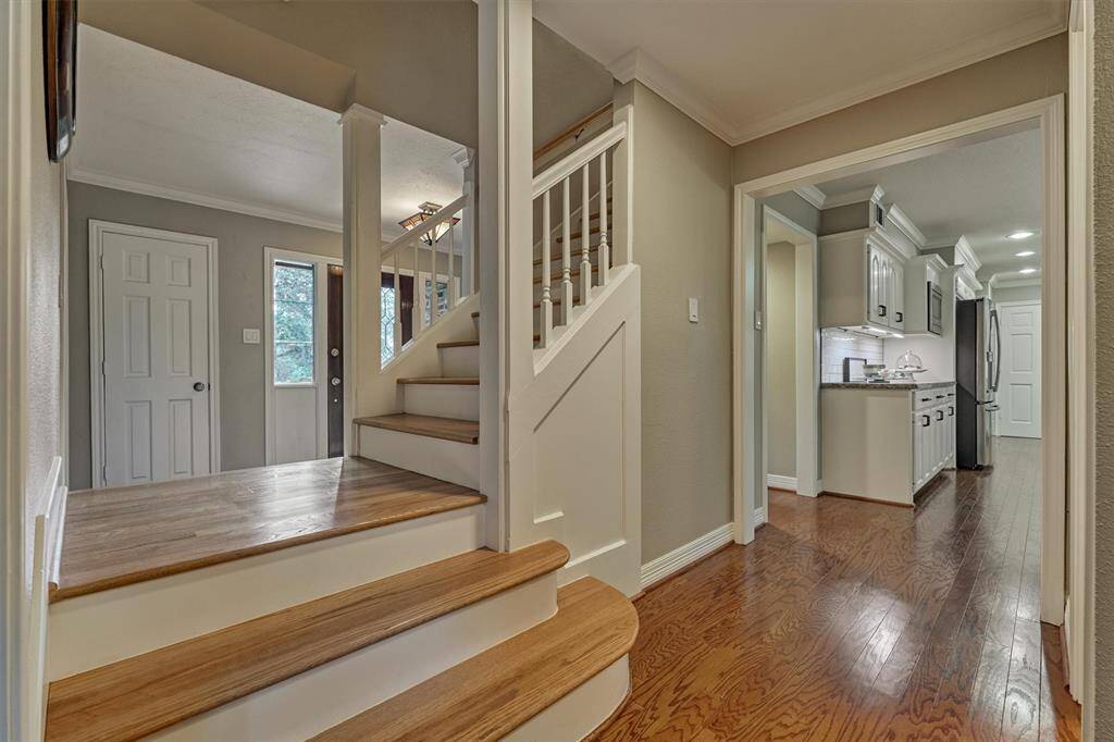 Lovely millwork on this wooden staircase leading to the upper level. To the right, there's a view of a modern kitchen with white cabinets and stainless steel appliances. The space has hardwood floors and neutral wall colors, creating a warm and inviting atmosphere.