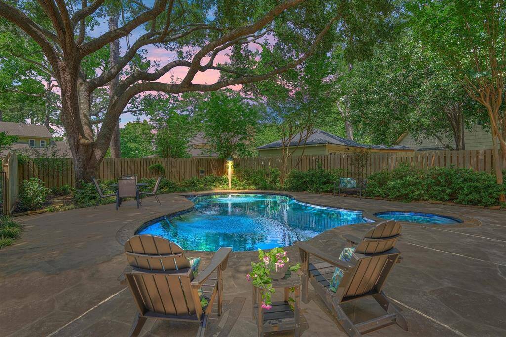This photo showcases a serene backyard with a beautiful pool surrounded by lush greenery and mature trees. There are comfortable seating areas and a cozy ambiance, perfect for relaxation and entertaining.
