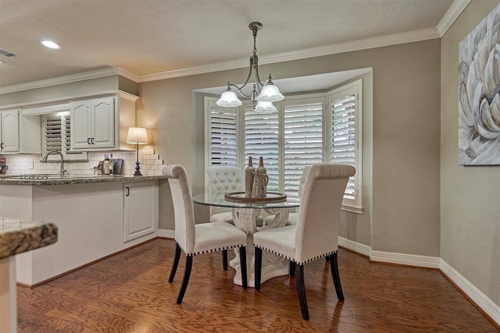 Charming bay window with shutters allows natural light to enhance the warm wood flooring and soft wall colors. Views of the pool and mature landscaping delight.