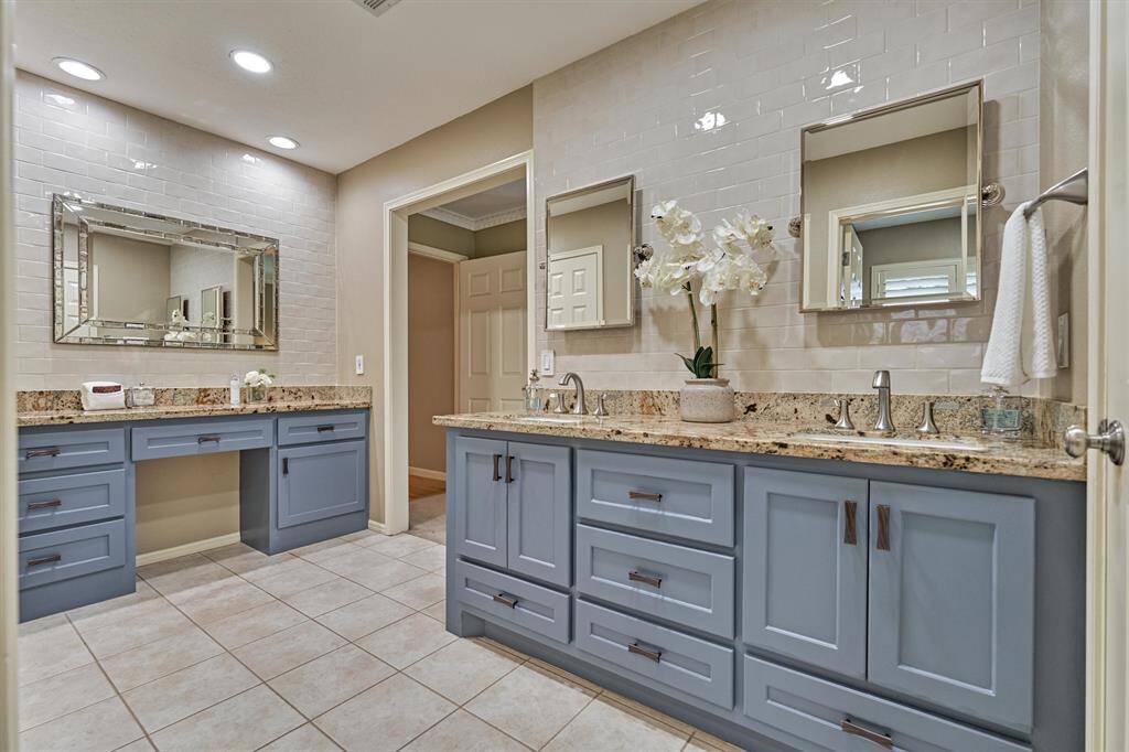 This spacious bathroom features dual sinks with granite countertops, cheery blue cabinetry, and large mirrors. Recessed lighting and neutral tiles add a modern touch, while the open layout provides functionality.