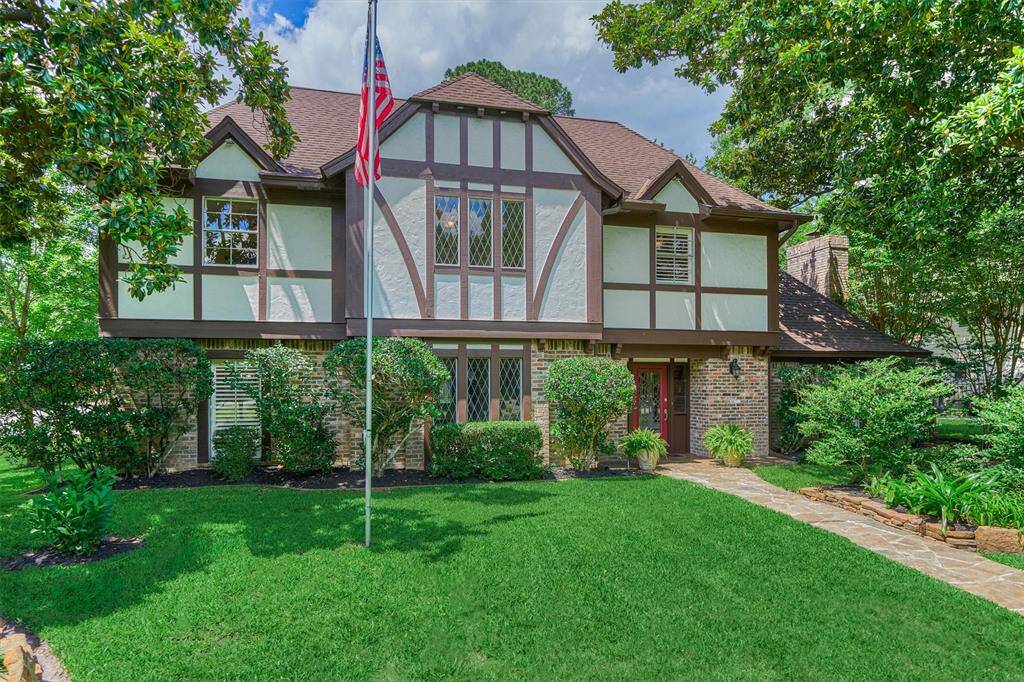 This charming two-story Tudor-style home features a well-maintained brick and stucco exterior, lush landscaping, and a welcoming pathway. The large windows and mature trees add to its inviting curb appeal.