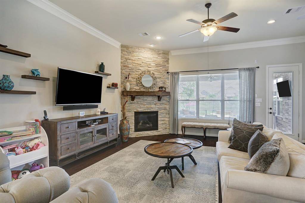 This home features large windows and a ceiling fan to provide a bright, airy feel. The open concept living room, just off of the kitchen, is painted in a neutral color scheme. It also has a stone fireplace, built-in shelves and crown molding.