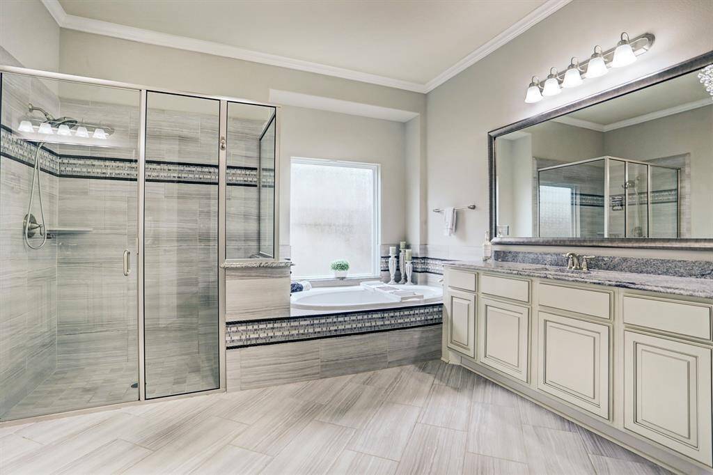 The bathroom in the primary suite is bright and modern, featuring neutral tones and large mirrors to enhance the room's brightness. The room is spacious enough to feature a walk-in shower, a corner bathtub, and dual-sink vanity.