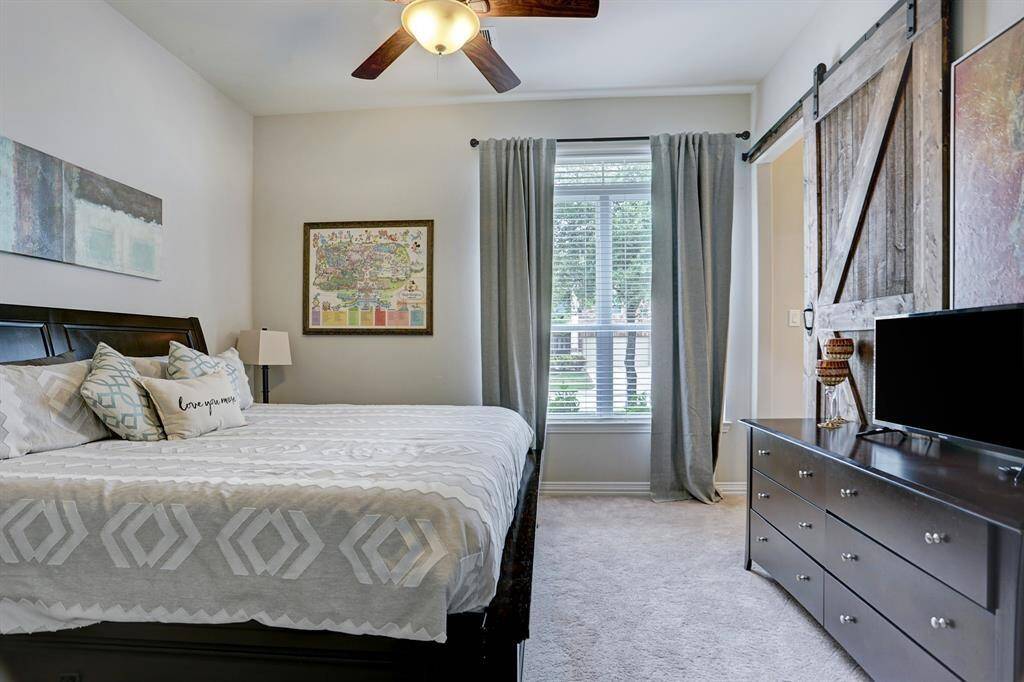 Secondary bedroom features a large window, high ceilings, a stylish barn door, and a ceiling fan. The room is well-lit with a large window and large closet (not shown).