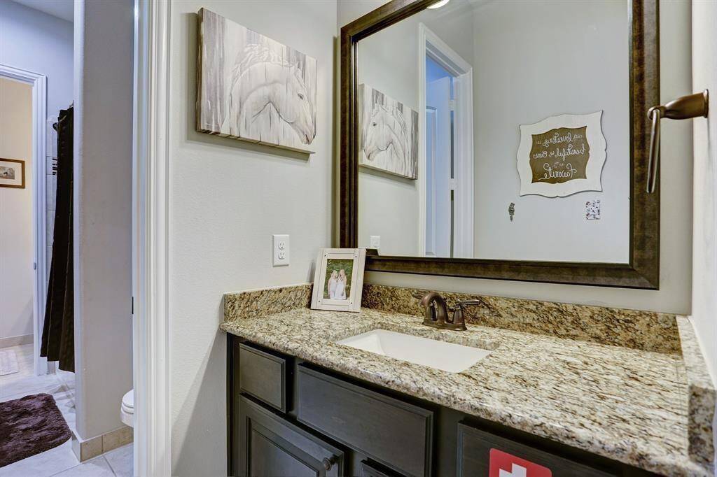 This bathroom features a granite countertop with a dark wood vanity, large framed mirror. It offers a clean, modern look with light walls and a spacious layout.