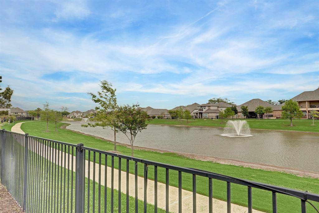Location, location, location! This photo showcases the water view from the backyard, which features a picturesque lake with a fountain and walking path. The area is lined with well-maintained lawns and houses, offering a peaceful and inviting atmosphere.