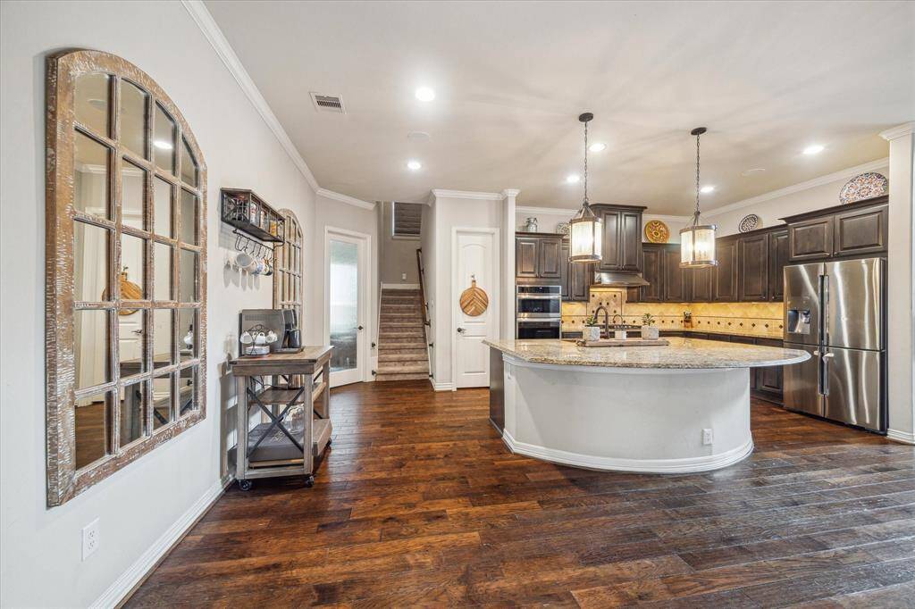 This kitchen features a spacious, open layout with a large island, pendant lighting, and dark wood cabinetry. Stainless steel appliances and granite countertops add a modern touch, while hardwood floors create a warm ambiance.