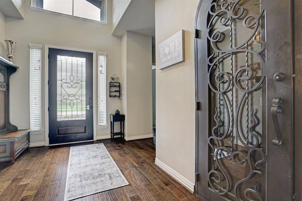 This inviting entryway features a stylish wrought iron door, elegant dark wood flooring, and abundant natural light from tall windows. Door to wine room is just off the entry way.