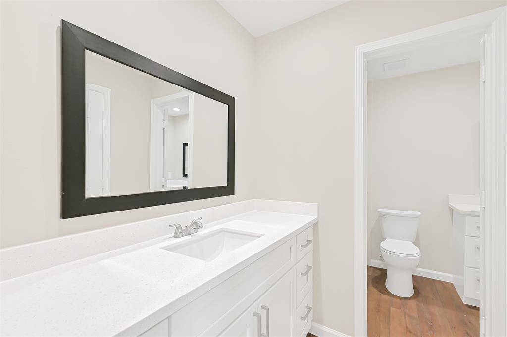 This primary bathroom boasts a clean, fresh look and offers a modern vanity topped with quartz counters, a large mirror, and white shaker cabinetry with polished nickel hardware.
