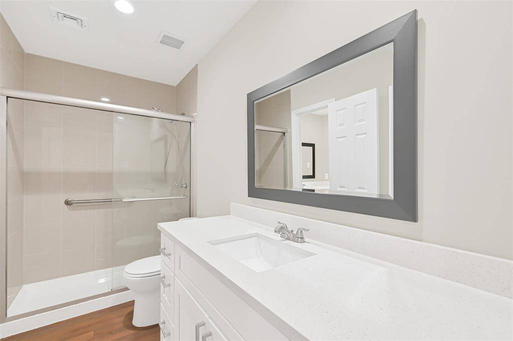 The well-positioned secondary bathroom features a single vanity with quartz countertops, a large decorative mirror, and a standing shower with a floor-to-ceiling tile surround and a seamless glass enclosure.
