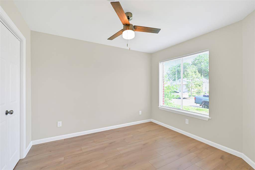 Secondary bedroom with neutral paint tones, a modern & energy-efficient ceiling fan, ample closet space, and views to the front yard through the oversized window.