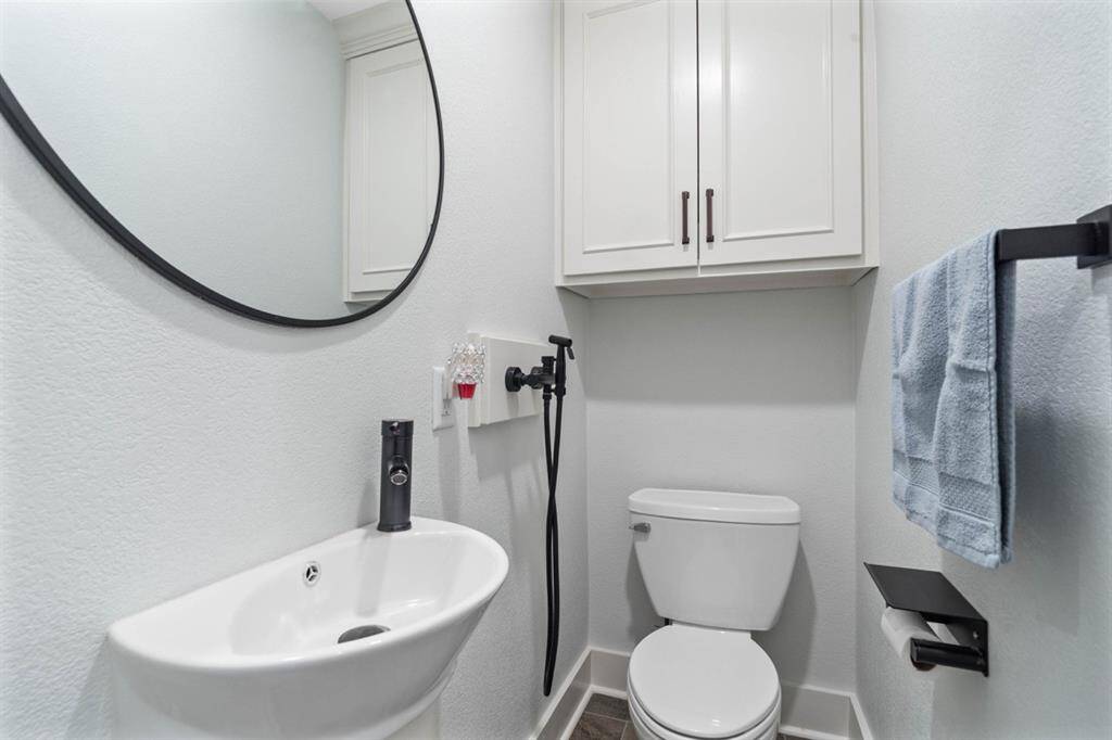 Half bathroom downstairs convenient for guests and features a pedestal sink, hand-held bidet and round framed mirror