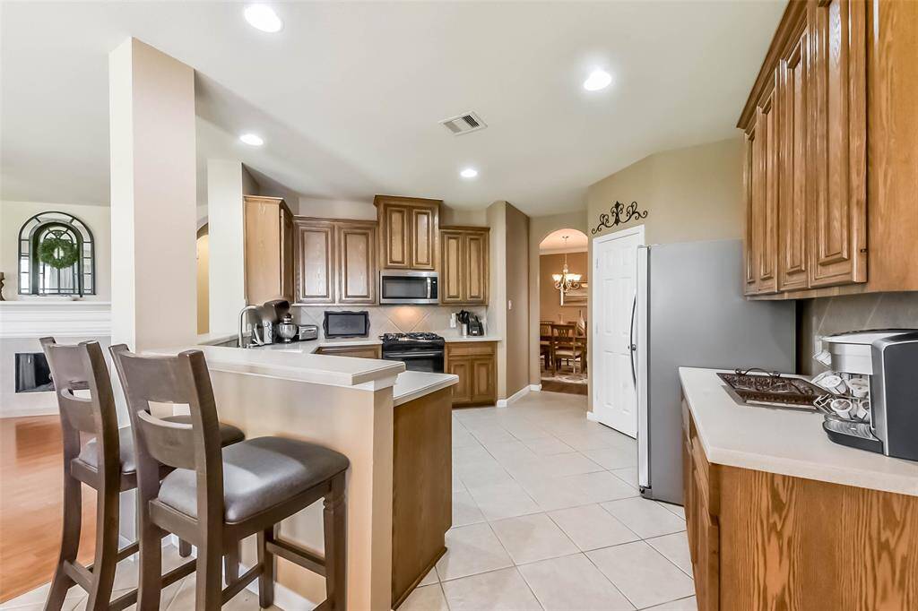 This kitchen features warm wooden cabinetry, modern appliances, and a breakfast bar with seating. It opens to a dining area, creating a spacious and inviting atmosphere.