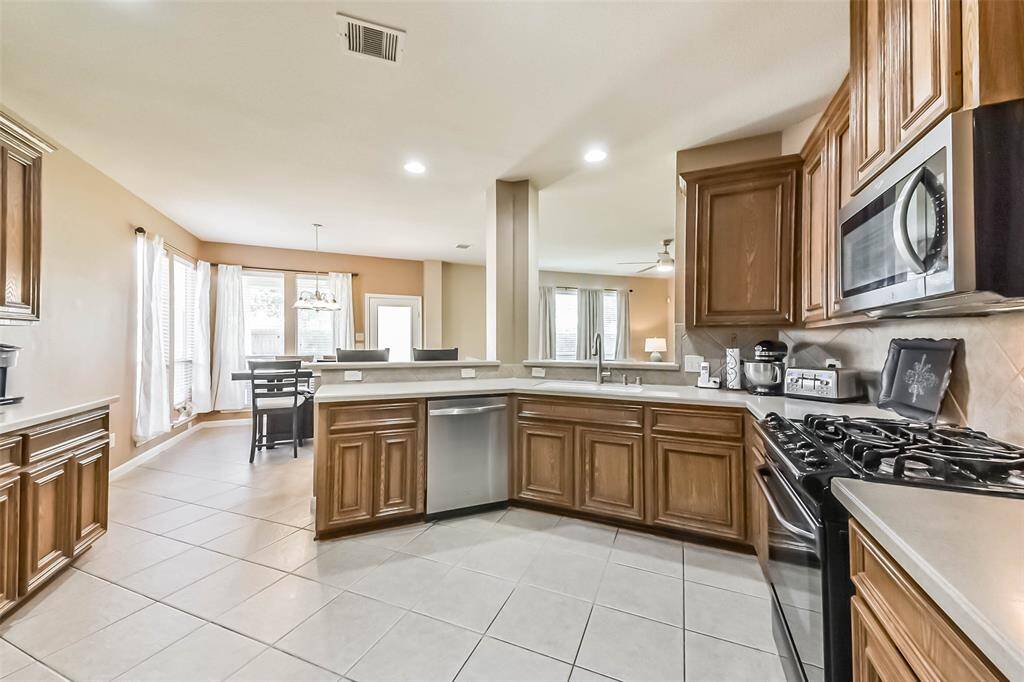 This spacious kitchen features wooden cabinets, stainless steel appliances, and gas stove.
