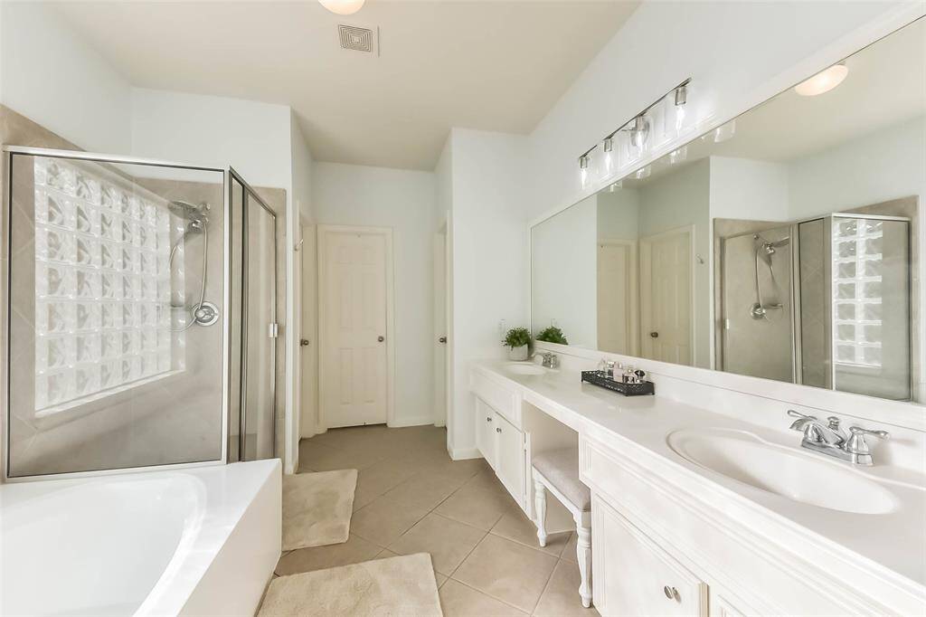 This bright, spacious bathroom features a large vanity with dual sinks, a glass-enclosed shower, a separate bathtub, and modern fixtures. The neutral tiles and ample lighting create a fresh, inviting atmosphere.