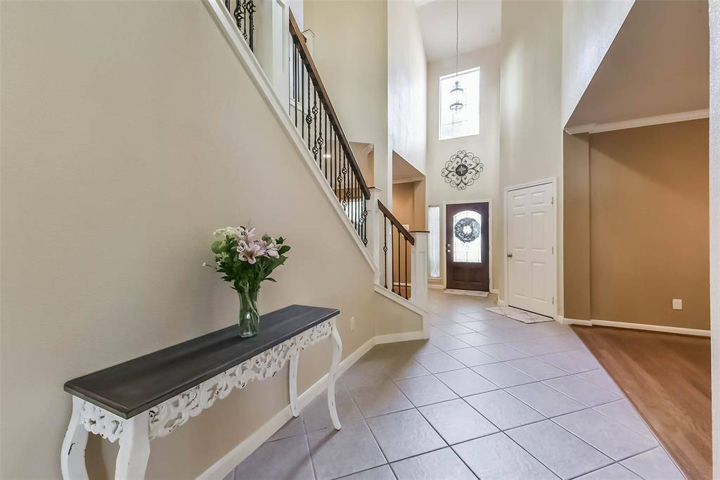Bright and inviting entryway with high ceilings and natural light. Features a decorative staircase, tiled floor, and a charming front door with sidelights. A perfect welcome to your new home.