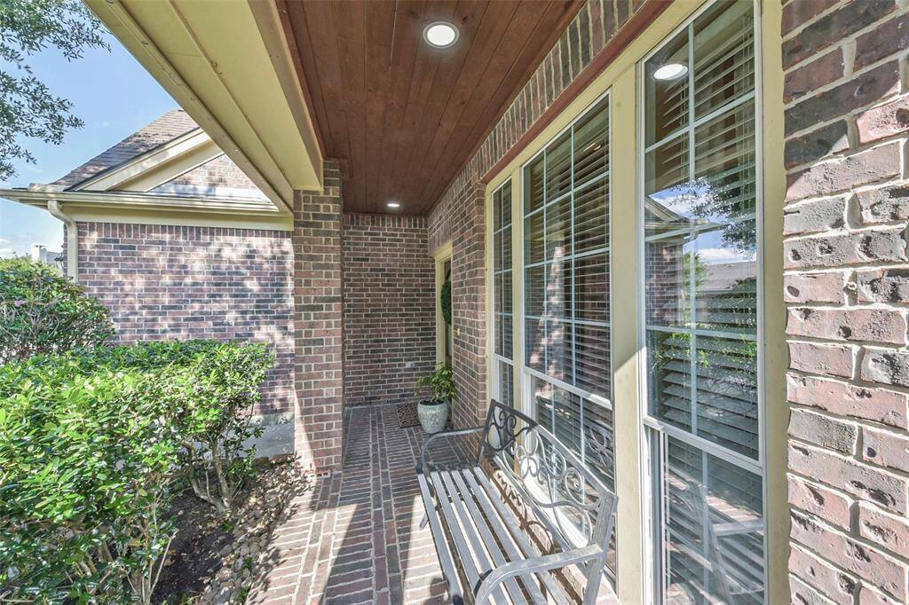 Charming brick front porch with a cozy bench, surrounded by well-maintained greenery. Features large windows for natural light and a welcoming entrance.