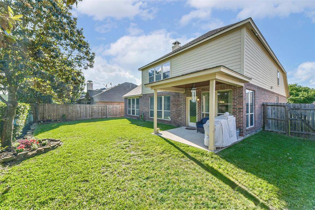 This backyard features a spacious lawn, a covered patio with seating, and manicured landscaping.