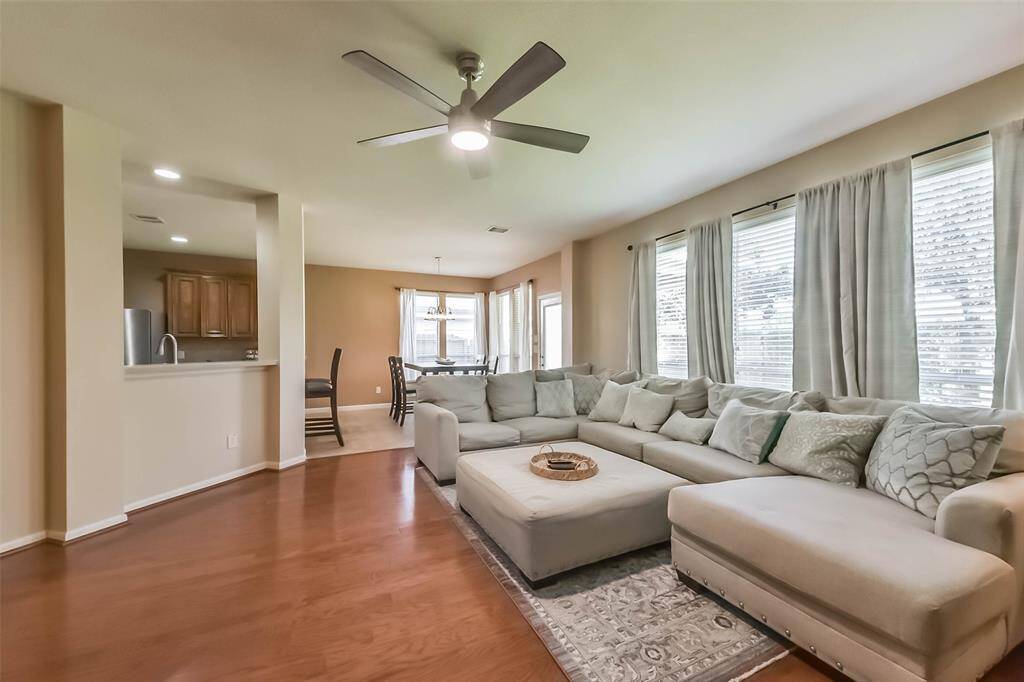 Bright and inviting living room with large windows and open floor plan leading to the dining area and kitchen. Perfect for entertaining and family gatherings.