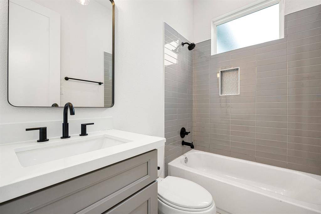 The secondary bathroom offers a refined, contemporary design with elegant light countertops and sleek, modern grey cabinetry. The oversized walk-in shower boasts a stunning custom tile surround, complemented by a decorative mirror that adds a touch of sophistication. With stylish tile floors, chic fixtures, and polished finishes throughout, this space is not only functional but also an inviting retreat.