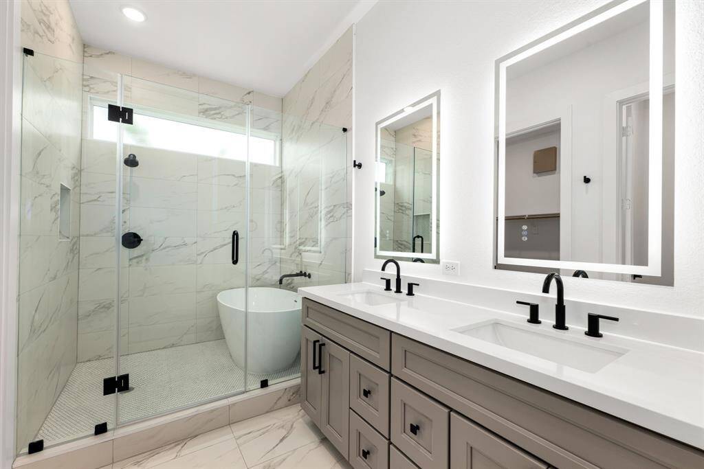 Indulge in spa-like luxury with this breathtaking primary bathroom, featuring an elegant double vanity with sleek quartz countertops, modern black fixtures, and illuminated mirrors. The stunning wet room design showcases a freestanding soaking tub and an oversized glass-enclosed shower adorned with marble-inspired tile.