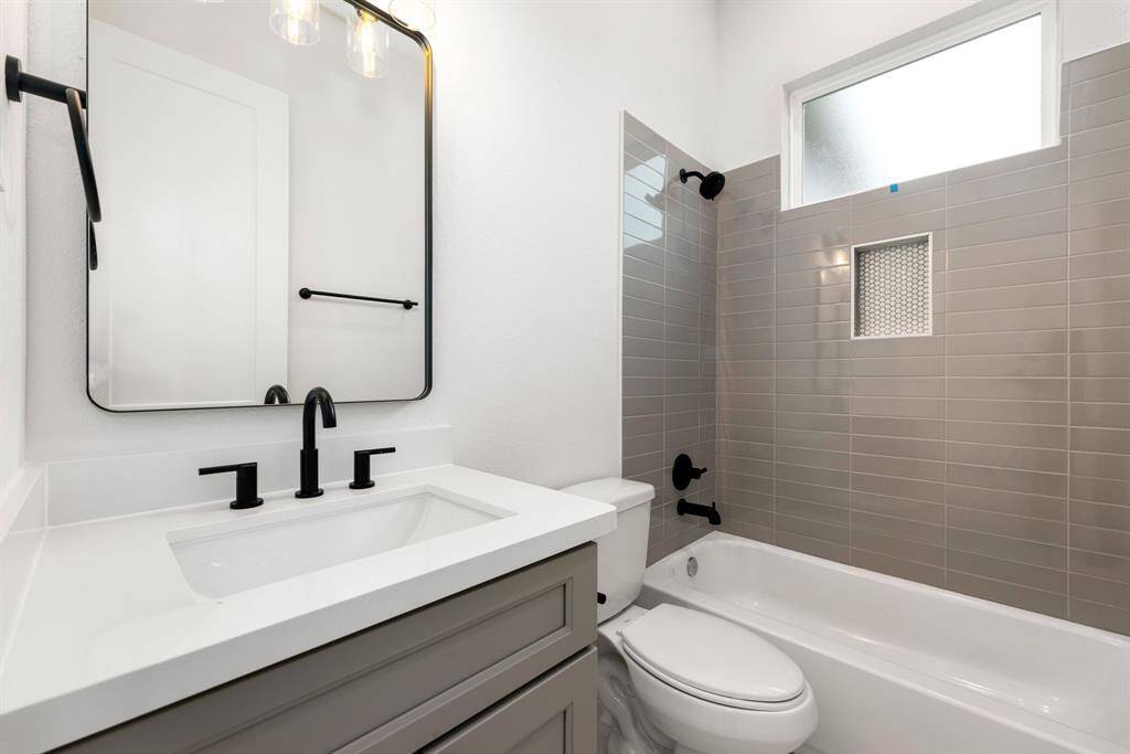 The secondary bathroom boasts elegant light countertops paired with contemporary grey cabinetry, creating a refined and airy atmosphere. The oversized walk-in shower, with its custom tile surround, offers a spa-like experience, while the decorative mirror adds a touch of sophistication. The sleek fixtures and modern finishes complement the tile floors, enhancing the bathroom’s sleek design.