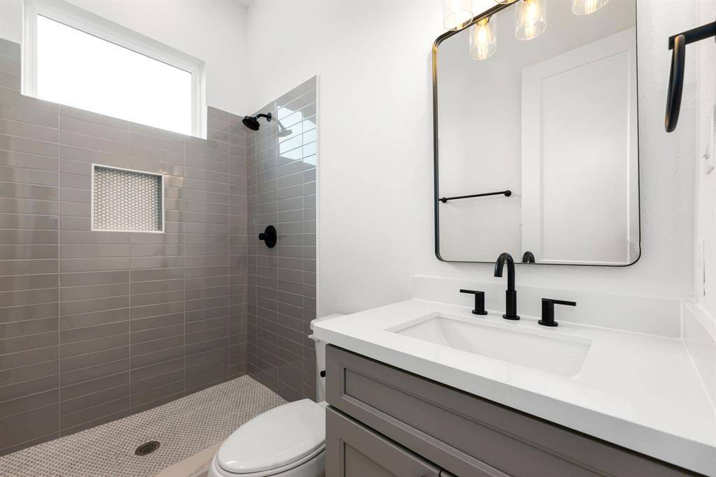 The secondary bathroom offers a refined, contemporary design with elegant light countertops and sleek, modern grey cabinetry. The oversized walk-in shower boasts a stunning custom tile surround, complemented by a decorative mirror that adds a touch of sophistication. With stylish tile floors, chic fixtures, and polished finishes throughout, this space is not only functional but also an inviting retreat.