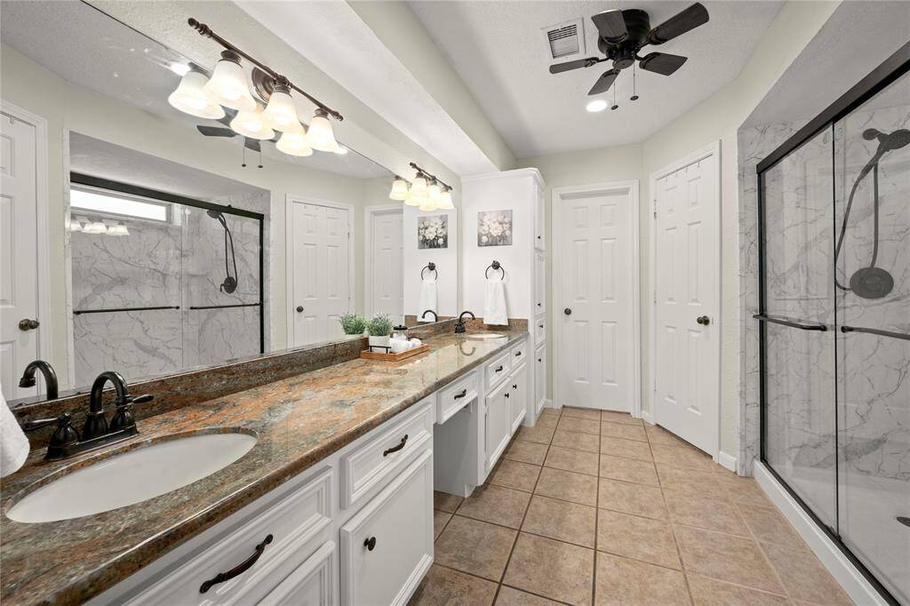 The primary ensuite bathroom has some amazing features. In 2025 the owners added this impressive walk-in shower with new fixtures, sliding glass doors and white and gray tile surround.  This retreat also possesses 2 walk-in closets, dual under-mounted porcelain sinks, granite countertops, updated lighting and plumbing fixtures. It also has extensive cabinetry under the countertops, a medicine tower and a vanity that allow for ample storage and personal space.