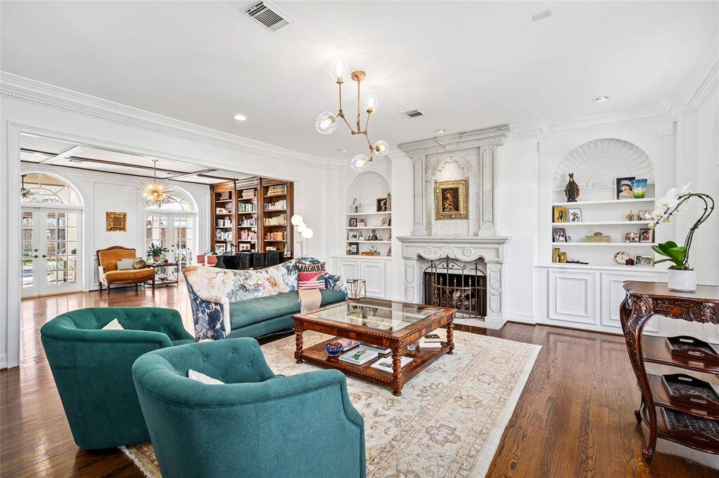 Elegantly appointed formal living room features custom carved limestone fireplace, high ceilings, crown molding, built ins with directional lighting, two arched windows and recessed lighting