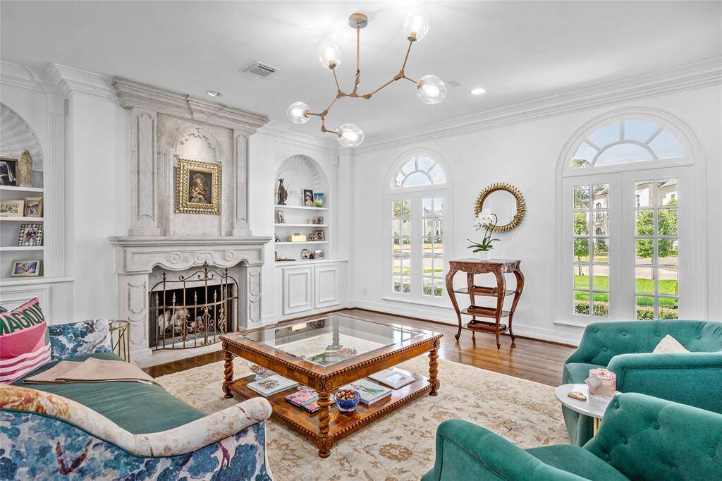 Elegantly appointed formal living room features custom carved limestone fireplace, high ceilings, crown molding, built ins with directional lighting, two arched windows and recessed lighting